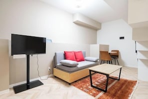 A modern living room with a sofa, a flat-screen TV, a coffee table, and a staircase.