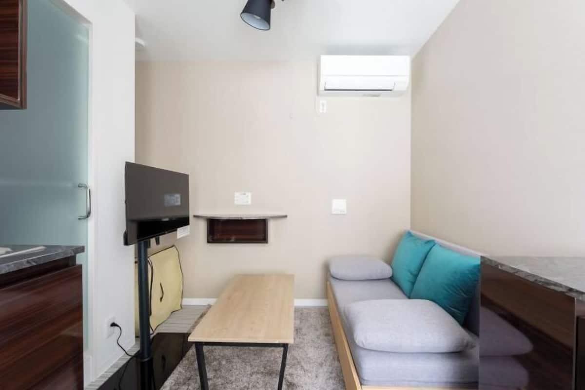 Una habitación pequeña y funcional con cama, escritorio, silla, televisor y estante.
