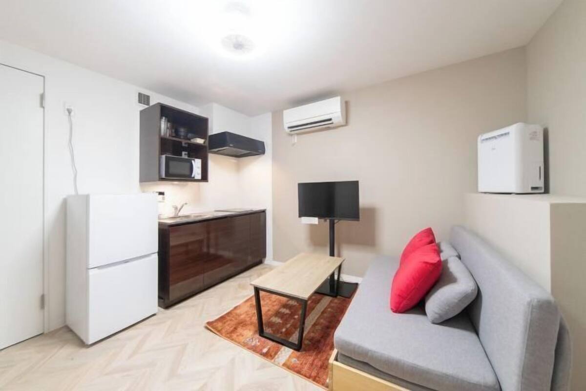Un espacio habitable compacto con kitchenette, un sofá, una mesita y un televisor.