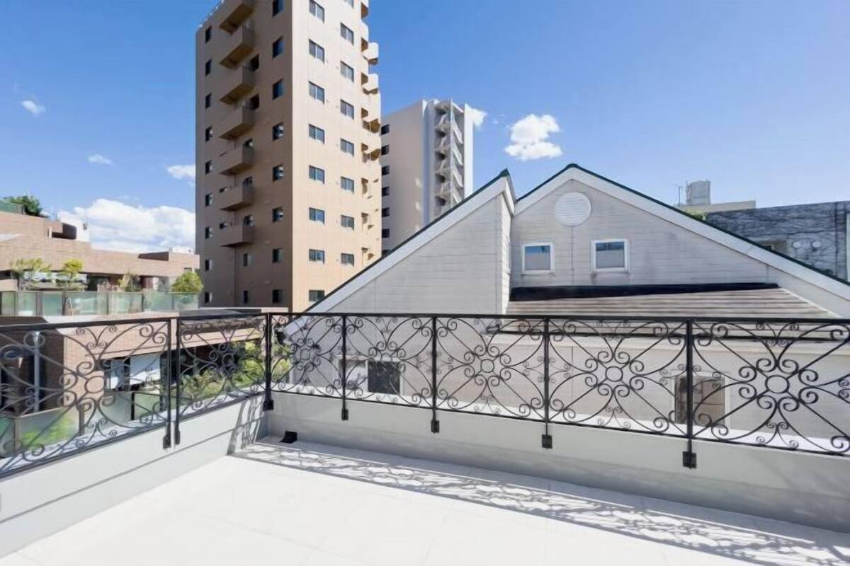 Una terraza en la azotea con barandilla de metal, un edificio con tejado a dos aguas y un cielo despejado.
