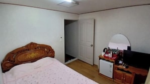 Une chambre à coucher avec un lit, un petit réfrigérateur blanc, une télévision et une armoire en bois.