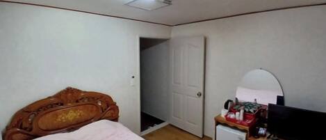 A bedroom with a wooden bed, a small refrigerator, a television, and a door leading to another room.