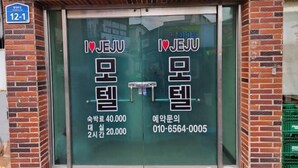 Une entrée d’immeuble avec deux portes en verre sur lesquelles figurent des inscriptions en coréen et un numéro de téléphone.