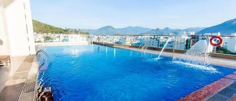 Una piscina con vistas a montañas, un puesto de salvavidas y un cartel de prohibido bucear.