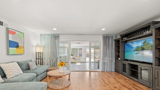 A modern living room with a sofa, a coffee table with flowers, a flat-screen TV, and a glass door leading to an outdoor area.