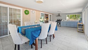 A dining area with a blue tablecloth, white chairs, and a kitchen in the background.