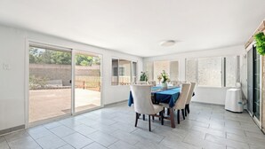 A spacious dining area with a table set for four, large sliding glass doors leading to an outdoor patio, and a white ceiling with a recessed light fixture.