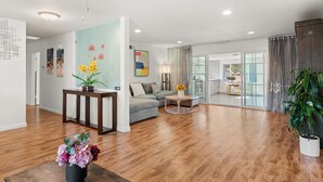 A spacious living room with hardwood flooring, a grey sofa, a coffee table, and a ceiling fan.