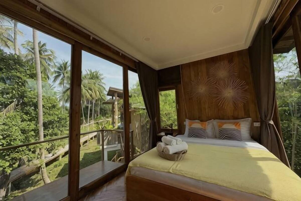A bedroom with a large bed, a view of the outdoors, and a wooden ceiling design.