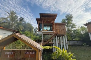 A wooden structure with a balcony, surrounded by greenery and palm trees. - Baan Proud Proud (Khanom)