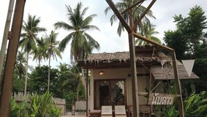 A wooden structure with a thatched roof, surrounded by palm trees and a pool.