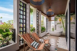 A modern bathroom with a large bathtub, two wicker chairs, and a view of the city.
