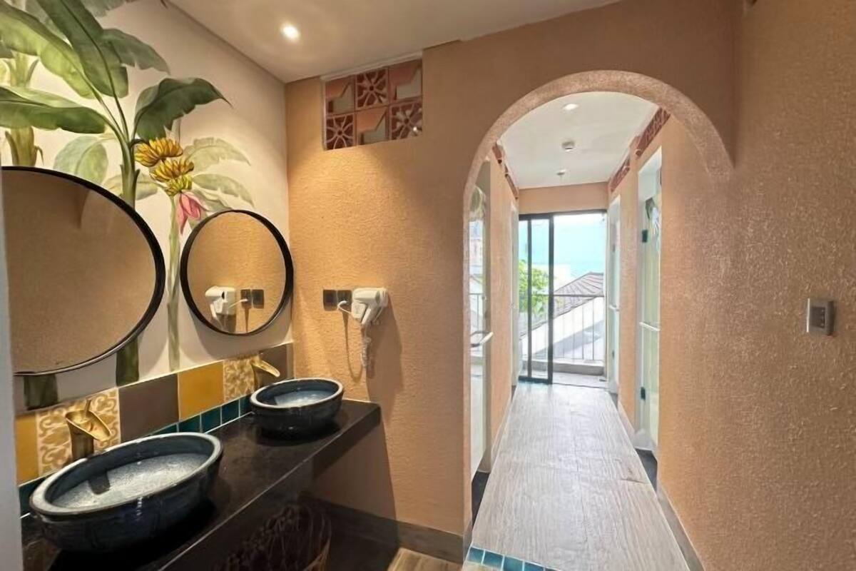 Casa de banho com duas pias pretas, um espelho grande e uma planta.