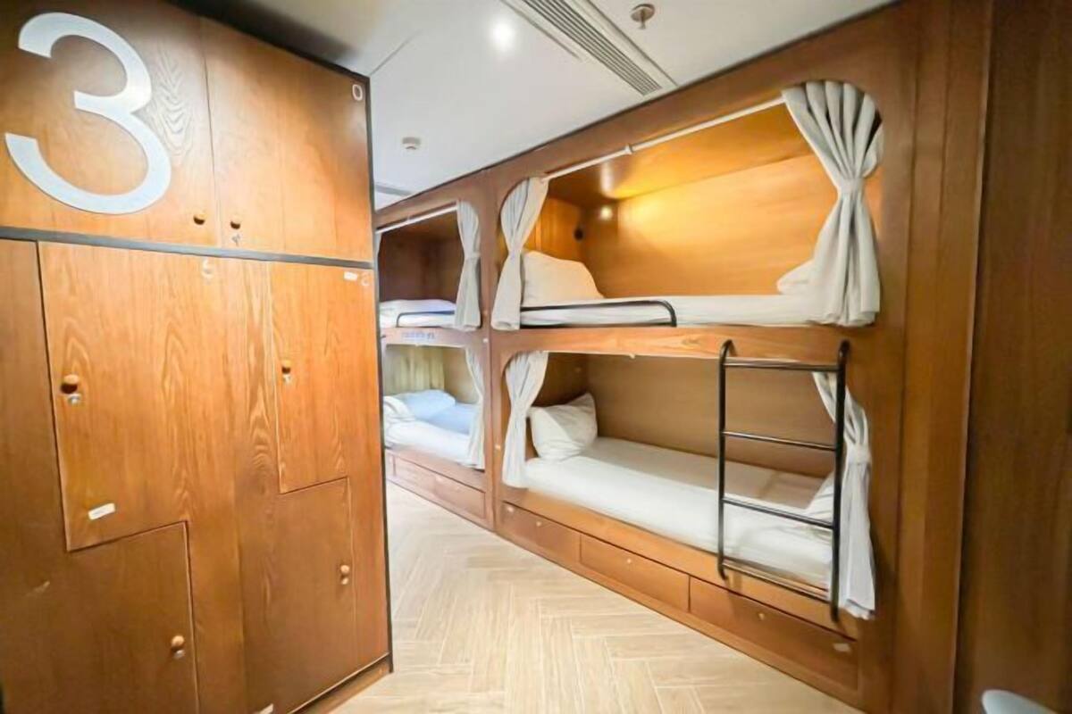 Um dormitório com paredes de madeira e uma placa com o número '3', com beliches com cortinas e uma escada.