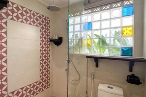 Ducha con puerta de vidrio, inodoro con manija de descarga y ventana con vidrios de colores.