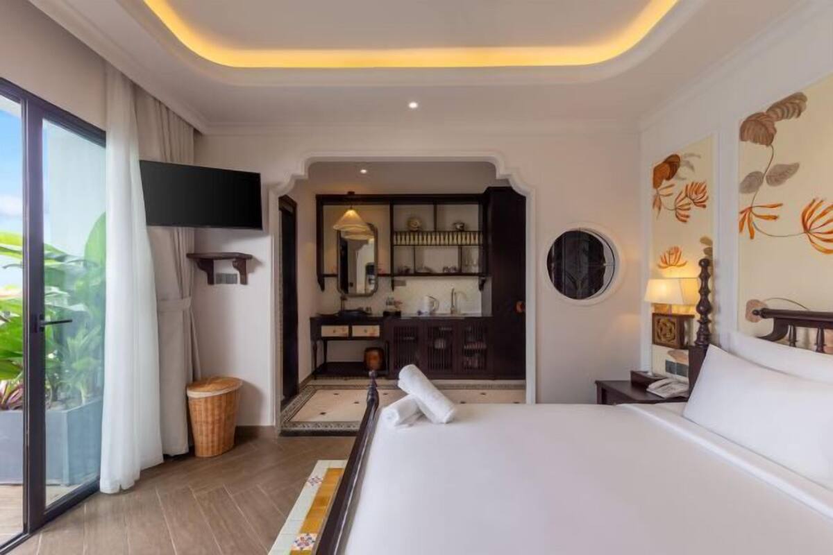 Quarto de hotel com cama, televisão, banheiro e vista para área verde.