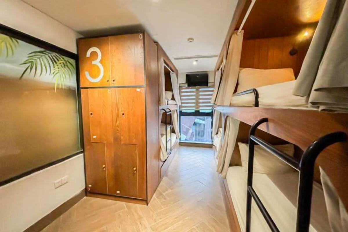 Interior compacto e bem iluminado com uma cama beliche, um guarda-roupa de madeira com uma placa com o número 3 e uma pequena área de estar.