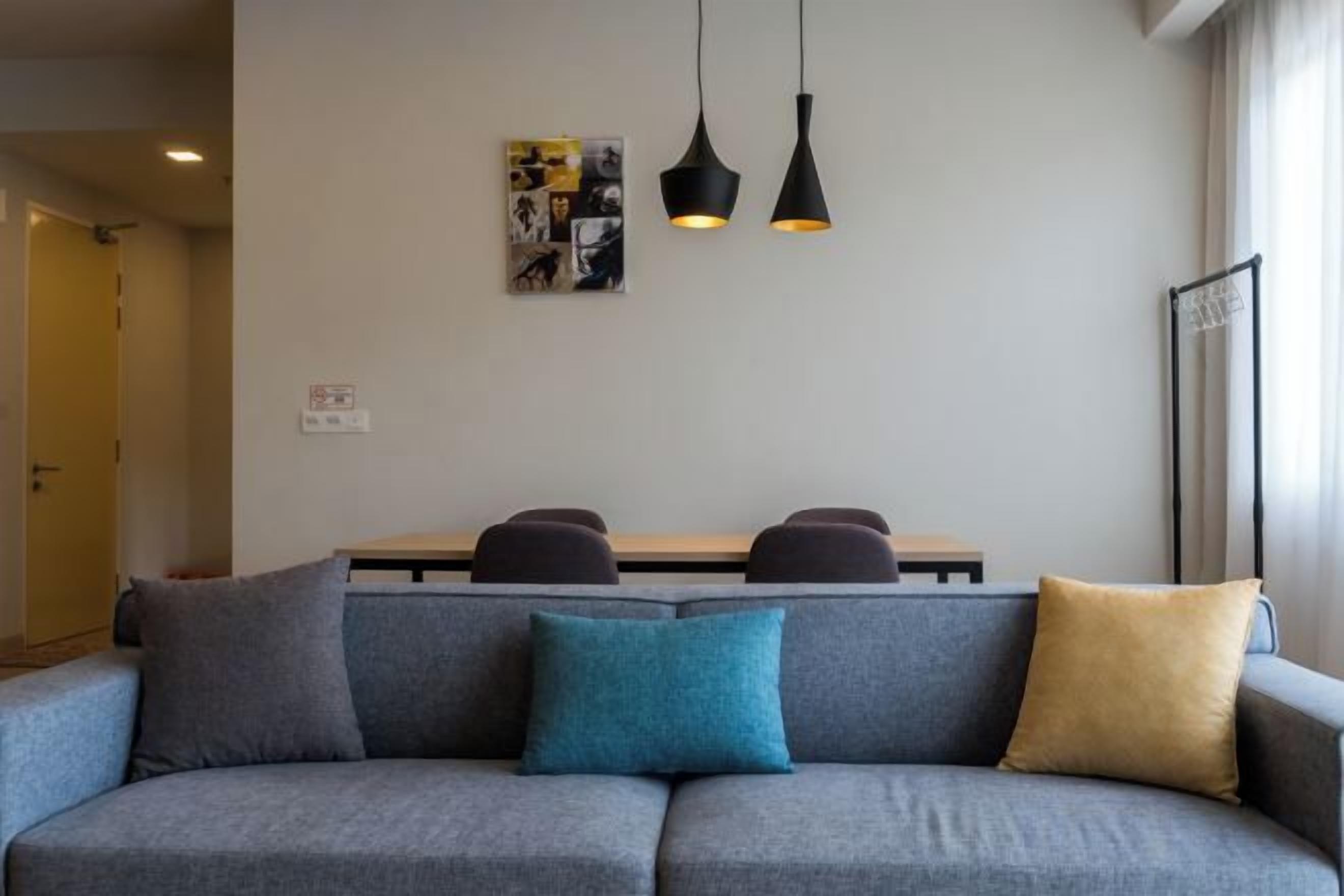 A gray sofa with three cushions, a dining table with chairs, and pendant lights.