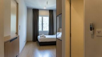 A hotel room with a bed, a wardrobe, a mirror, and a window with curtains.