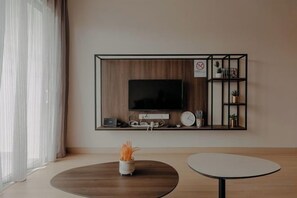 A modern living room with a flat-screen TV mounted on a wooden panel, a small shelf with decorative items, and a round coffee table. - Windmill Upon Hills By Rapi (Genting Highlands)