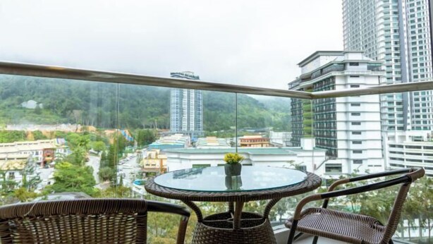 A balcony with wicker furniture, a glass table, and a view of a cityscape with buildings and greenery. - Windmill Upon Hills By Rapi (Genting Highlands)