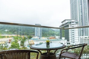 A balcony with a round table and wicker chairs, overlooking a cityscape with buildings and greenery. - Windmill Upon Hills By Rapi (Genting Highlands)