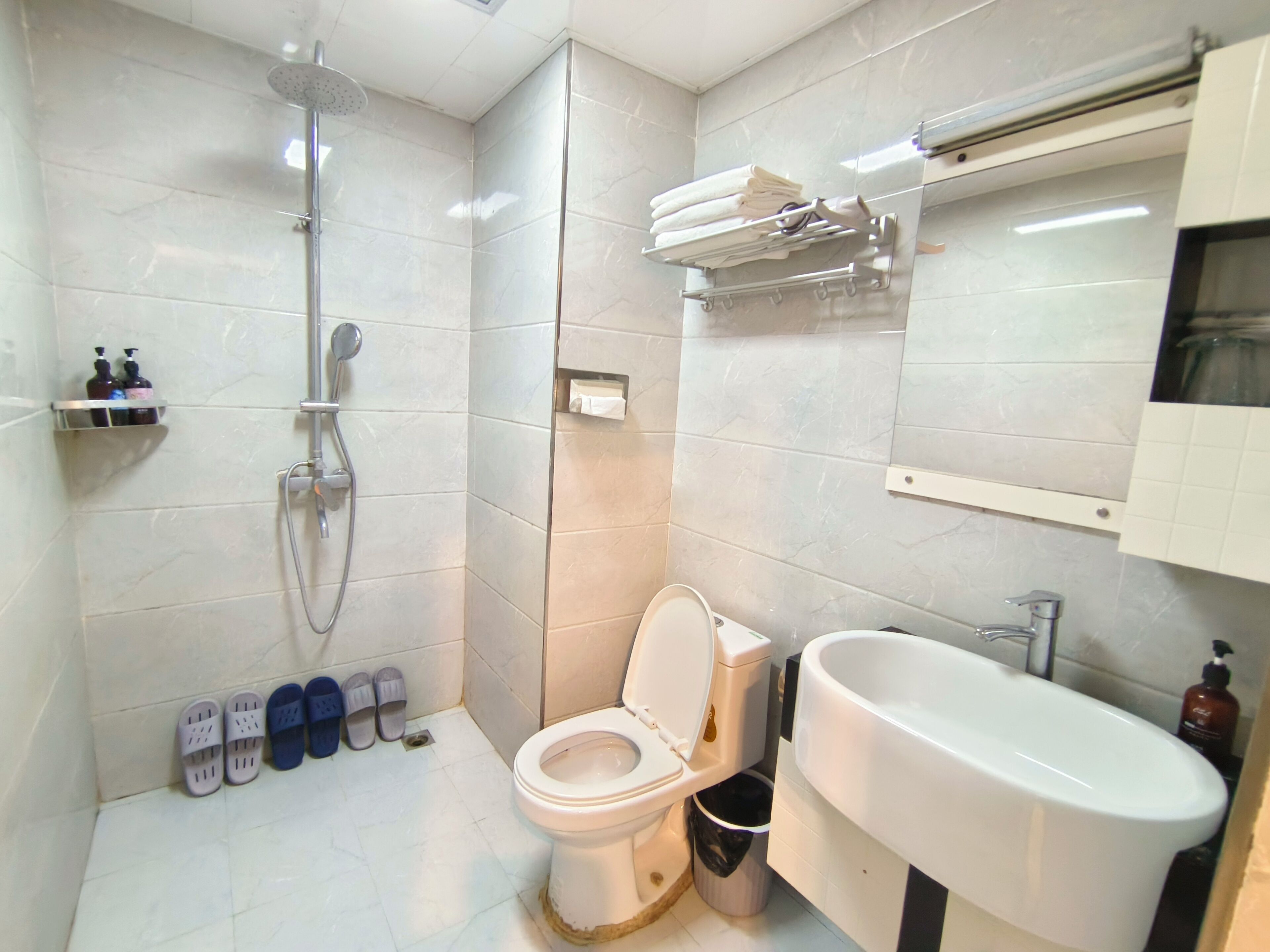 A bathroom with a toilet, sink, and shower. There are slippers and toiletries on the floor.
