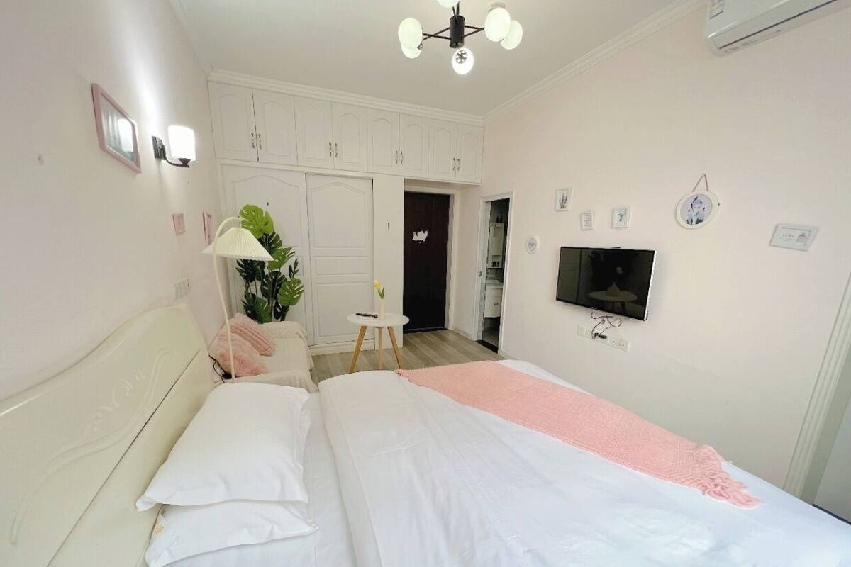 A bedroom with a bed, a bedside table with a lamp, a TV mounted on the wall, and a wardrobe.