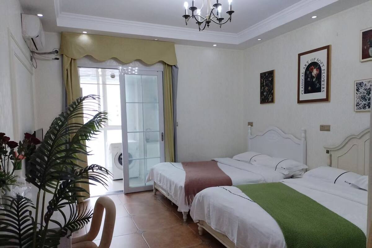 A hotel room with two beds, a dining area with a chair, and a large window with curtains.