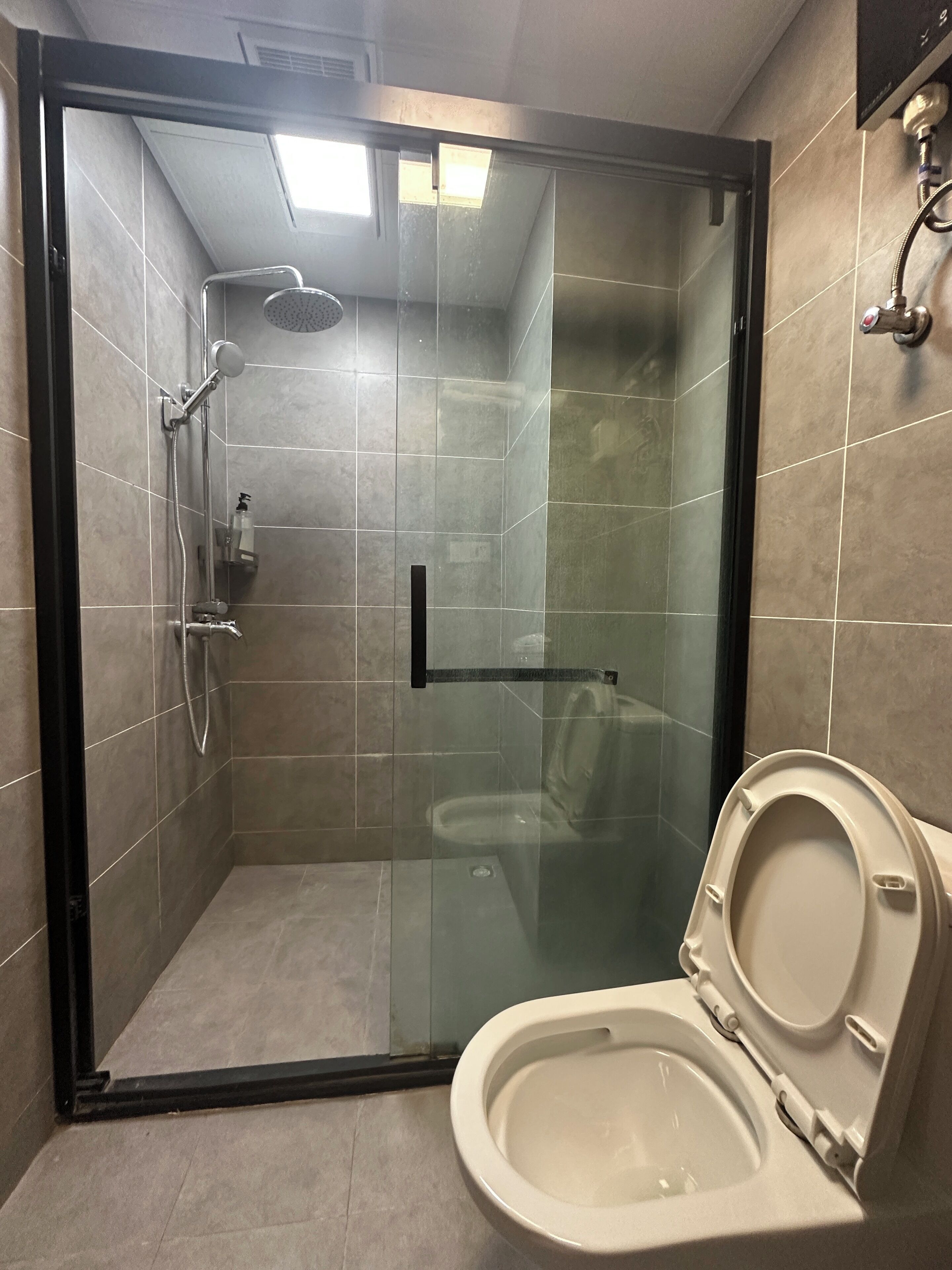 A modern bathroom with a glass-enclosed shower, a toilet, and a hand dryer.