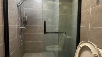 A modern bathroom with a glass-enclosed shower, a toilet, and a hand dryer.