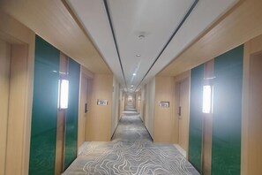 A hotel corridor with doors on both sides, a patterned carpet, and overhead lighting. - XINGHAI HOTEL AND RESORT (Boten)