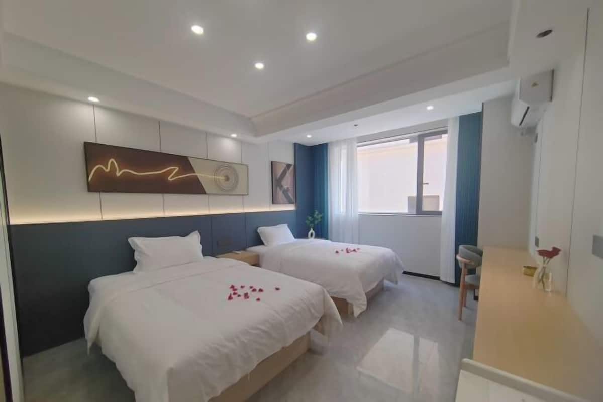 A hotel room with two beds, a modern light fixture, a window, and a desk.