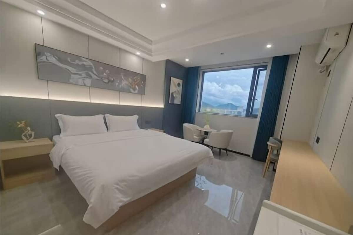 A modern hotel room with a large bed, a desk, and a window offering a city view.