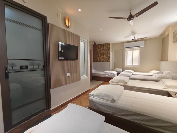 Habitación de hotel con cuatro camas, televisión, ventiladores de techo y un ventanal grande.