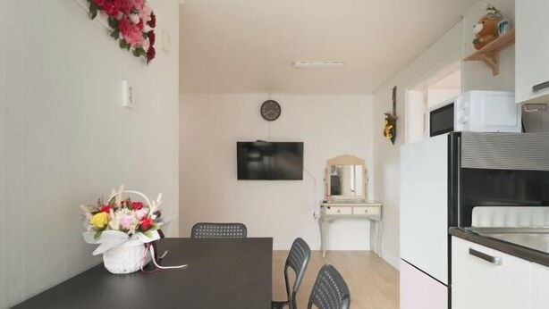 A dining area with a dark wooden table, black chairs, and a small white basket with flowers. There is a flat-screen TV mounted on the wall above the table. - Seoul Full House/Hongdae Entrance Sta.Exit 7. Party room. Big House. Two Rooms. (Seoul)
