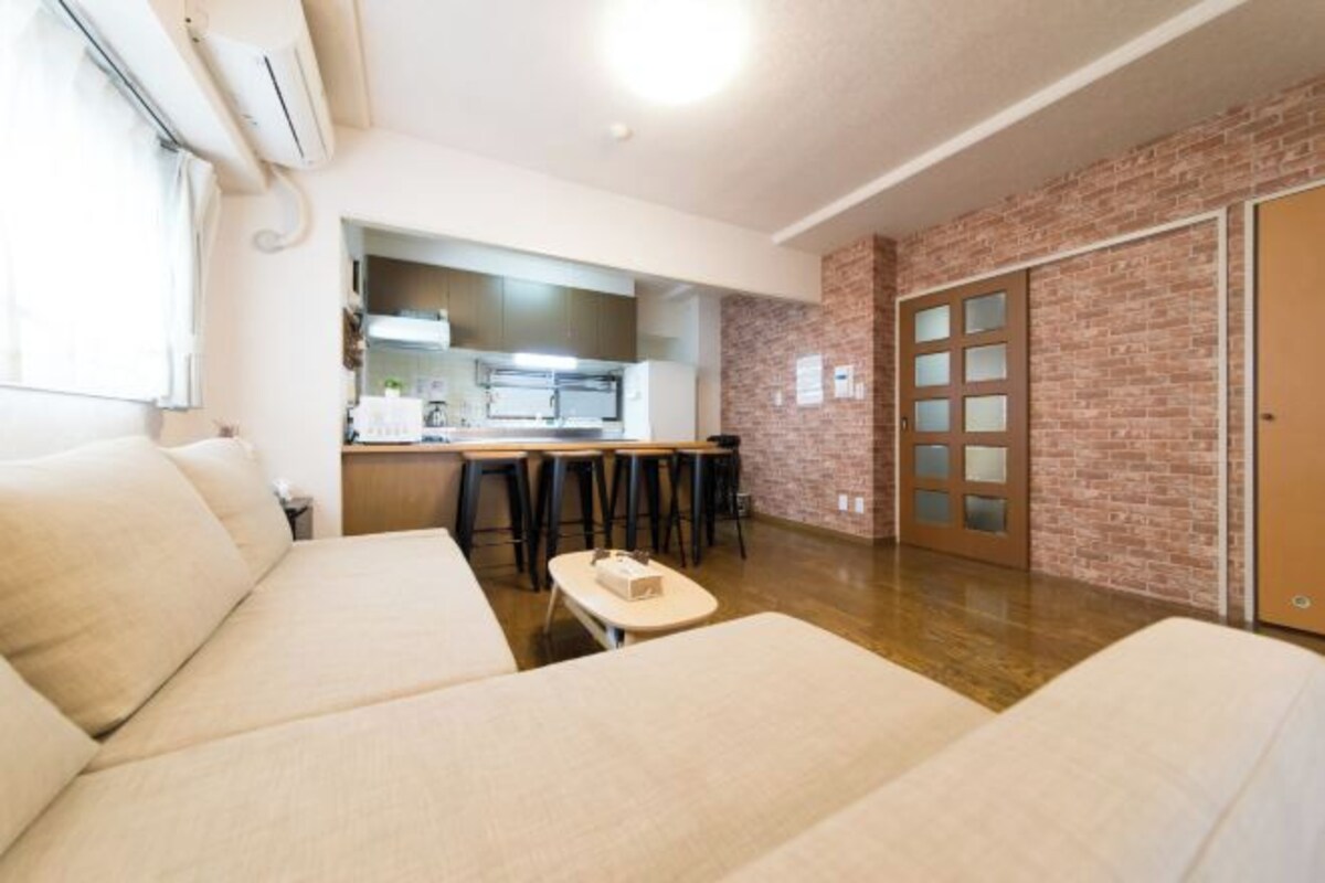 Una habitación de hotel moderna con kitchenette, zona de comedor y pared de ladrillo decorativa.