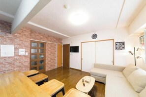 Habitació amb paret de maó, mobles de fusta, un sofà, una televisió i un rellotge.