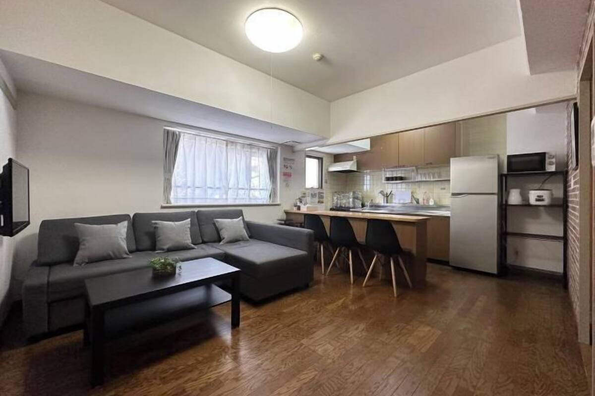 A compact living space with a sofa, a dining table, a kitchen area with a refrigerator, microwave, and a small island.