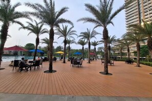 An outdoor patio area with palm trees, tables, and umbrellas. - Gold coast seaview pik Jakarta by SuiteStay (North Jakarta)