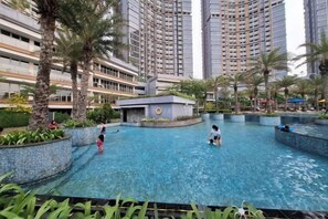 Zona de piscina rodeada de altos edificios residenciales, palmeras y una pequeña estructura de diseño circular.