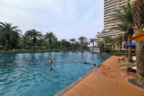 A swimming pool with palm trees and a wooden deck. - Gold coast seaview pik Jakarta by SuiteStay (North Jakarta)
