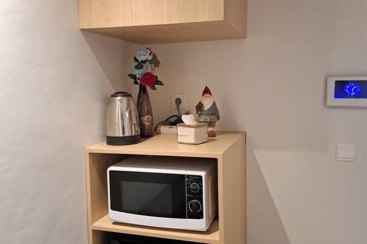 A microwave on a shelf with a small clock and decorative items on a wooden cabinet.
