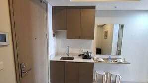 A modern kitchen with a built-in island, a sink, and two stools. - Gold coast seaview pik Jakarta by SuiteStay (North Jakarta)