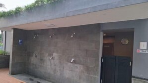 A covered outdoor shower area with multiple showerheads, a sign indicating a toilet, and a wooden deck. - Gold coast seaview pik Jakarta by SuiteStay (North Jakarta)