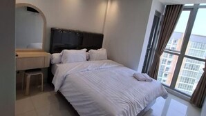 A modern hotel room with a large bed, a desk, and a window with curtains. - Gold coast seaview pik Jakarta by SuiteStay (North Jakarta)