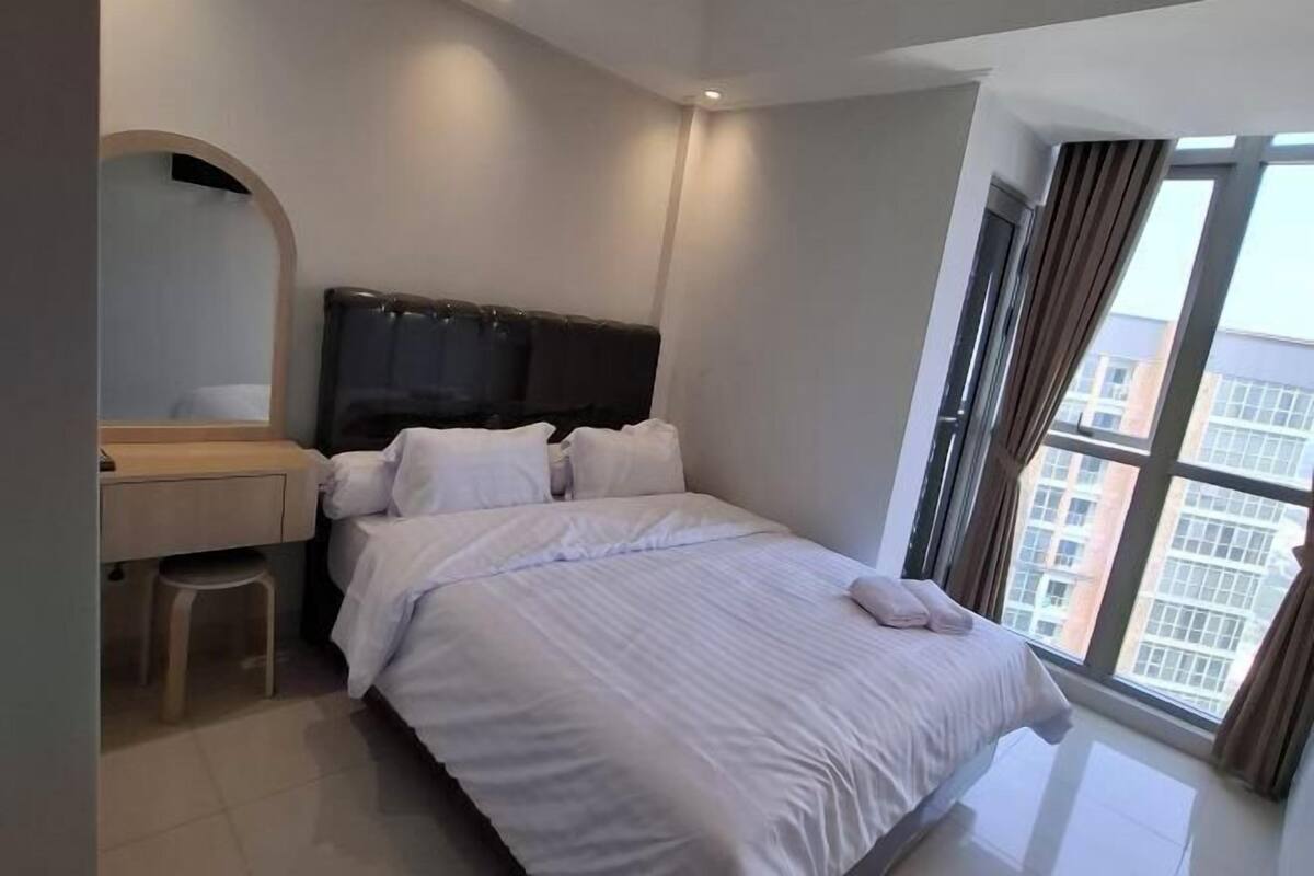 A modern hotel room with a large bed, a desk, and a window with curtains.