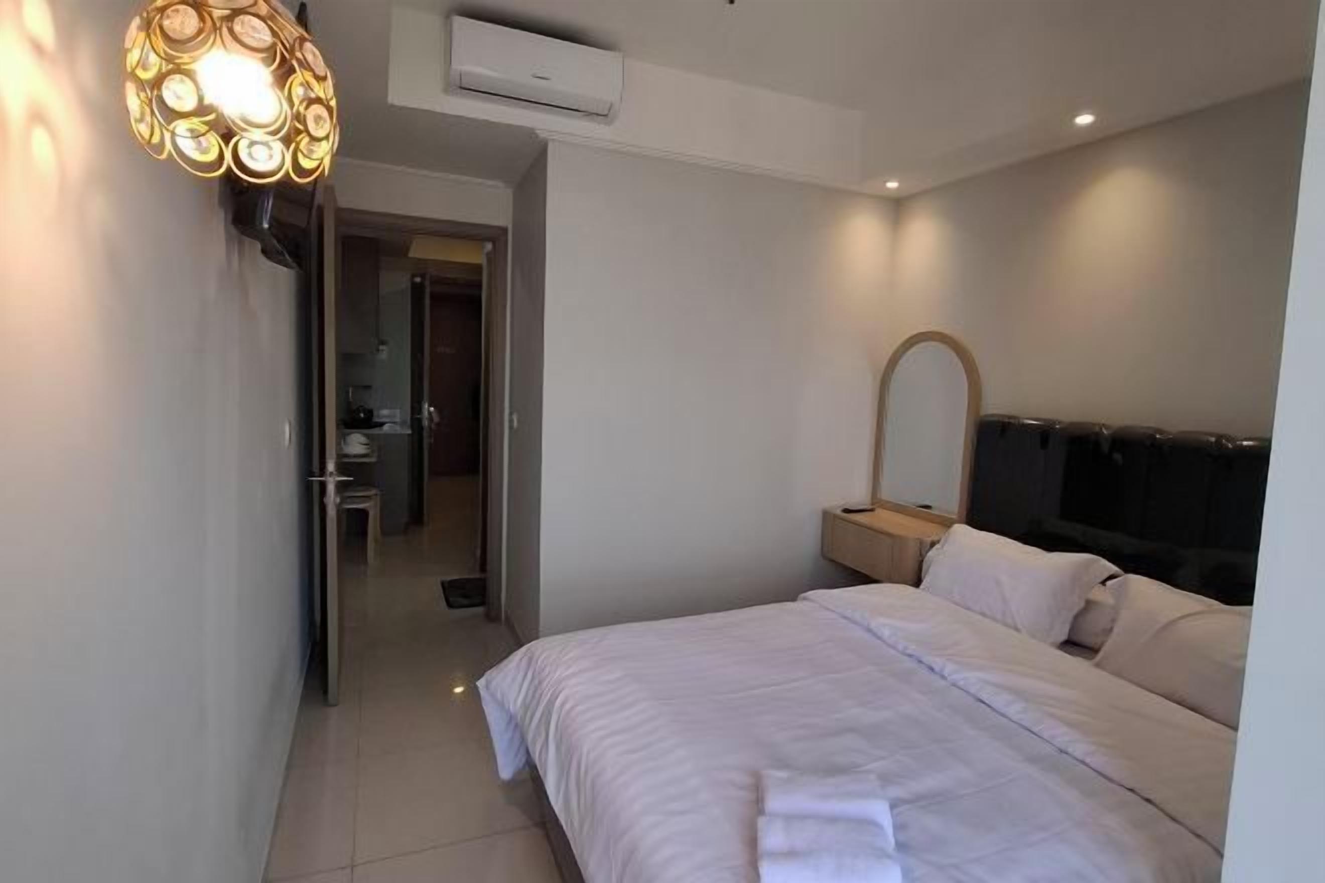A modern hotel room with a large bed, a bedside table, a mirror, and a wall-mounted TV.