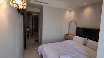A modern hotel room with a large bed, a bedside table, a mirror, and a wall-mounted TV.