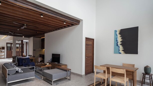 A modern living room with a sofa, a TV, a wooden dining table, and a painting on the wall. - Baan Kamana Guest House (Takua Thung)